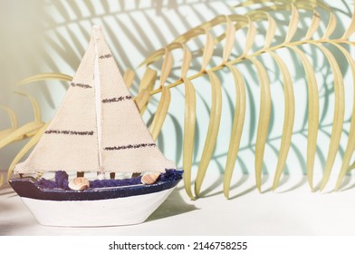 Small Miniature Toy Sail Boat, Tropical Palm Leaves With Shadows Background, Sunny Soft Pastel Light Tones. Simplicity Beach Styled Home Traveling Decor, Happy Day Summer Beach Vacation. 