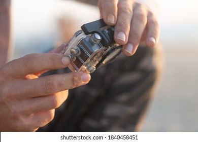 Small Modern Action Camera In Waterproof Housing Filming In Shallow Water On Beach, Man Holding Recording Equipment Sitting Outdoors. Selective Focus