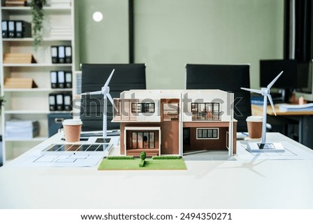A small modern house scale model on an office desk, surrounded by green energy elements like wind turbines and solar panels, sustainable renovation and various rooms in an eco-friendly design.