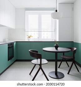 Kleine und moderne Küche mit stylischem Terrazzo-Fußboden, angesagtem, schwarzem Esstisch mit zwei Stühlen und stylischen weißen und grünen Wänden und Schränken
