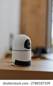 A small modern security camera sits on a wooden table in a bright home setting, suggesting monitoring and safety. Concept for home surveillance, privacy, and everyday tech use in daily life.