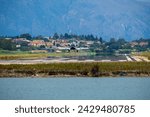 Small modern white business jet  landing at Corfu Ioannis Kapodistrias international airport. Mountain with trees and houses at the background.