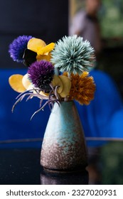 Small multi coloured composition with thistles in a blue vase. Cafe table decoration.