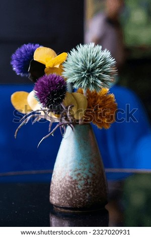 Small multi coloured composition with thistles in a blue vase. Cafe table decoration.