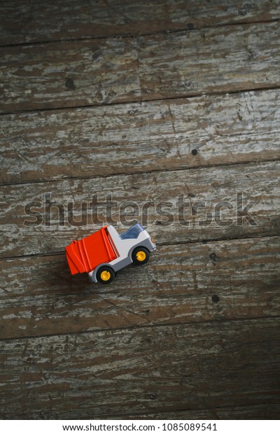 A small multi-colored toy truck lies on a wooden\
rustic floor.