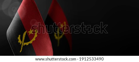 Small national flags of the Angola on a dark background