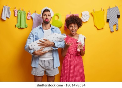 Small Newborn Daughter Sleeps Comfortably In Fathers Embrace. Tired Couple Care About Infant. Upset Dad With Diaper On Head, Holds Baby Wrapped With Blanket. Irritated Mother Going To Feed Kid