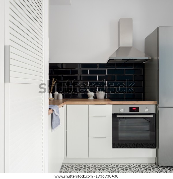 Small and nice kitchen with white cupboards,\
drawers and wardrobe, black wall tiles, wooden countertop and\
silver kitchen appliances