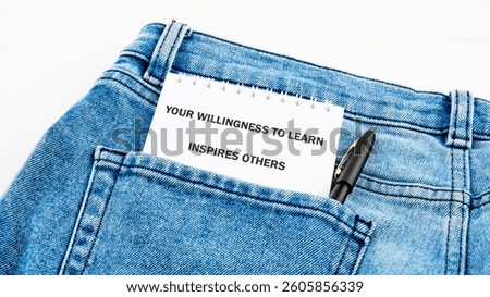 A small notepad with an inspiring message is placed in the back pocket of a pair of blue denim jeans. The message reads your willingness to learn inspires others, highlighting the value