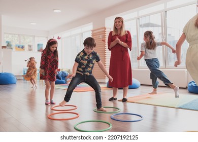 Small nursery school children with female teacher on floor indoors in classroom, doing exercise. Jumping over hula hoop circles track on the floor. - Shutterstock ID 2207192125