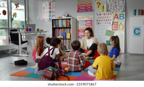 Small nursery school children with teacher sitting on floor having lesson. Young woman teach preschool kids in classroom sitting on floor together - Powered by Shutterstock