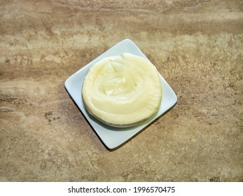 A Small Oaxaca Cheese Round Or Wheel On A White Plate.