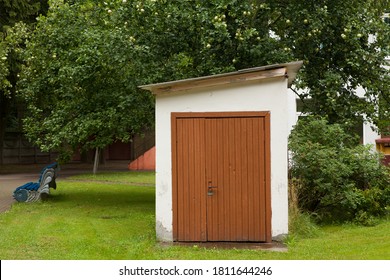 Small Old Neat Brick White Outbuilding Barn And Brown Wooden Door In The Hospital Courtyard Garden In Summer.