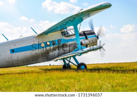 Small old private plane standing in spring fields by blue sky. White personal retro crop duster still in summer meadow befor flight. White retro airplane on green airfield at summer sun light day