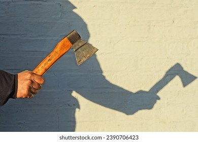 small old sharp dangerous iron industrial rusty with a wooden handle iron hatchet in hand near a white wall on the street with the shadow of a man's silhouette in the sun