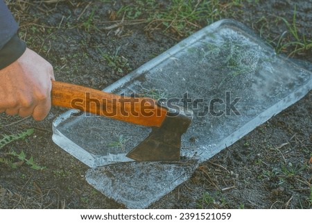 a small old sharp dangerous iron industrial rusty with a wooden handle with a hatchet in his hand breaks a piece of frozen ice on the ground during the day on the street in winter
