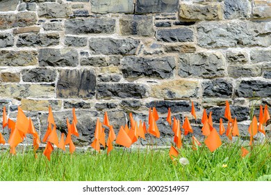 Small orange flags places in grass in memory of the thousands of Indigenous children that died in Canada's residential school system. Wide view.
