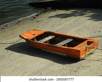 A Small Orange Wooden Dinghy On The Beach Sand