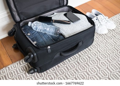 Small overnight weekender black suitcase with wheels packed with clothes, water, essentials for a short getaway lying on timber floorboards at home ready to go