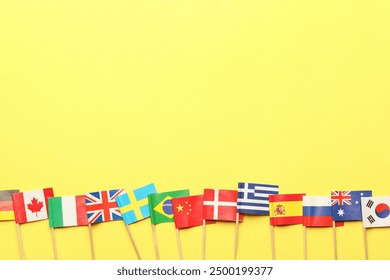 Small paper flags of different countries on yellow background, flat lay. Space for text