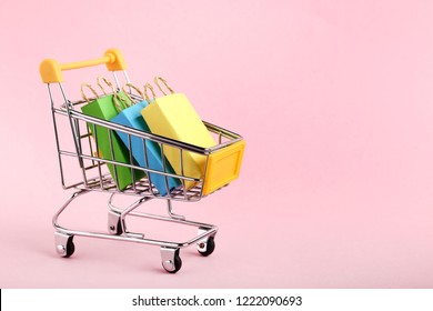 Small paper shopping bags with shopping cart on pink background - Powered by Shutterstock