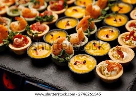 Small pastry shells are filled with a bright yellow sauce and topped with a cooked shrimp. The tartlets are neatly arranged in rows.