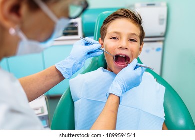 A small patient with an open mouth at a dentist appointment in a modern clinic. Hands of unrecognizable pediatric dentist doing examination procedure for smiling cute boy in hospital.