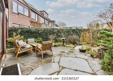 Small Patio With Gray Armchairs And Wooden Table With Green Hedge