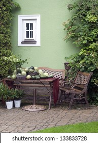 Small Patio Or Street Garden With Rustic Chair And Table, Green Vegetable And Plants.