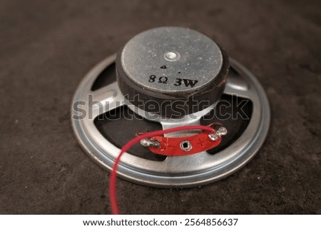 Small PC speaker with the text "8 ohm 3 watt" on the magnet, placed on a dark table back up