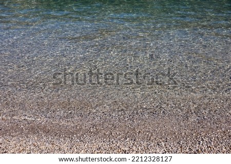 Small pebble stones on sea beach with transparent water. Background for coast vacation