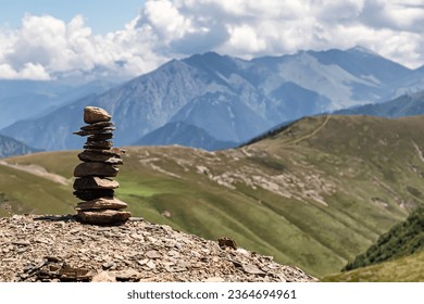 Small pebbles are made up in a tower and keep the balance, personify balance and tranquility. In the background, mountain slopes and clouds