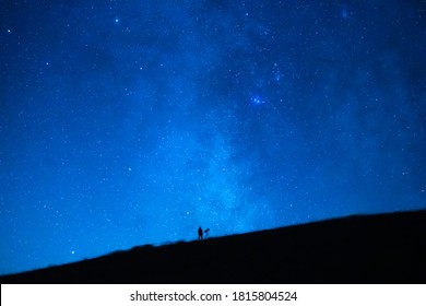 Small person observing the immensity of the universe and the stars. Silhouette of an astronomy lover with a telescope observing the blue starry sky at night.