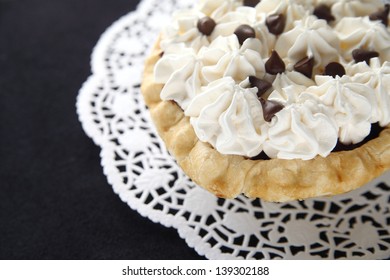 Small Pie With Whipped Cream And Chocolate Chips On A Doily