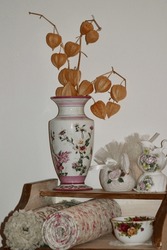 A Small Piece Of Furniture With Chinese Lantern Flowers In A Vase.
