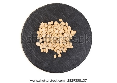 A small pile of roasted peanuts is presented on a round, dark grey slate serving board against a clean white background.