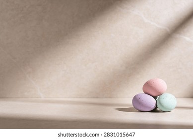 A small pile of three speckled Easter eggs in soft pastel colors rests on a textured surface, illuminated by gentle light and shadow patterns