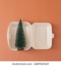 Small pine tree inside white food container. Minimal contemporary art concept about ecology, consumption and festive symbolism. Fine art still life reflecting modern lifestyle and seasonal meaning.