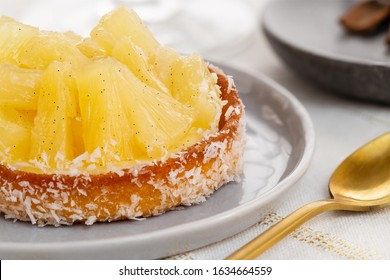 Small pineapple tart or tartlet with glazed pineapple fruit pieces and grated coconut by a golden spoon, over a white and gold table cloth. - Powered by Shutterstock