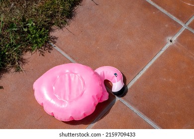 small pink flamingo float deflated on the edge of a swimming pool