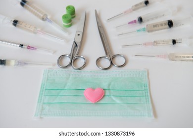 Small Pink Heart Placed On The Mask With A Syringe And Surgical Scissors Placed Around And Tourniquet On White Background.Health Care.