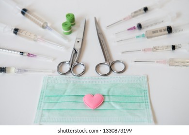 Small Pink Heart Placed On The Mask With A Syringe And Surgical Scissors Placed Around And Tourniquet On White Background.Health Care.