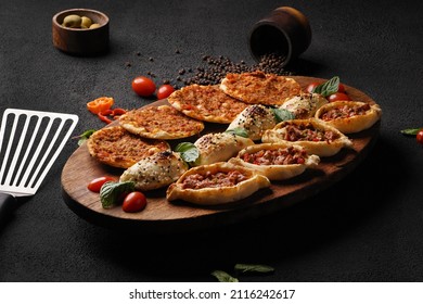 Small Pizza With Mozzarella Cheese, Sausage, Ham, Parsley, Lettuce, Cherry Tomatoes In The Olive Wood Planks On A Dark Black Wooden Background                  