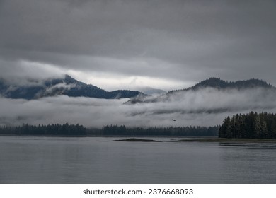 A small plane is captured flying over a tranquil body of water with an abundance of white, fluffy clouds in the background