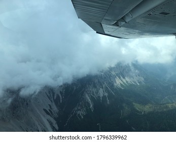 Small plane wing with view of rocky mountaintops covered in thick white clouds below it at the border auf Austria and Slovenia