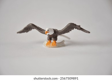Small plastic figurine of a bald eagle perched on a white background.