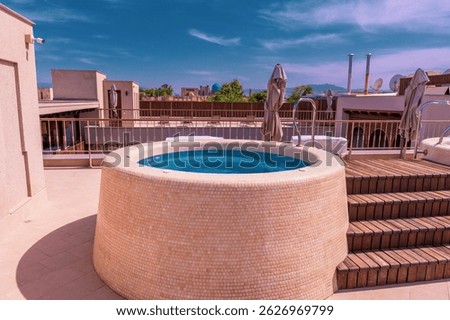 A small pool with a blue top is on a roof. The pool is surrounded by a stone wall