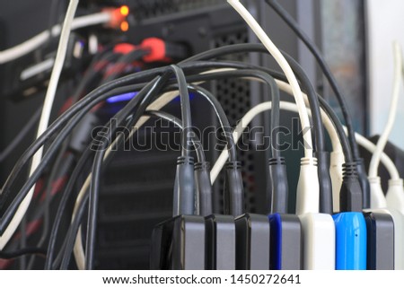 Small portable hard drives in stack connected to rear PC backup digital computer data. external hard disk with usb cords messing office space. 