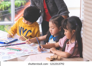 Small Pre School Student Kids Color Painting On Paper In Art Group Classroom In A Playroom With A Teacher Guiding On The Background, For Children Day School Education Concept