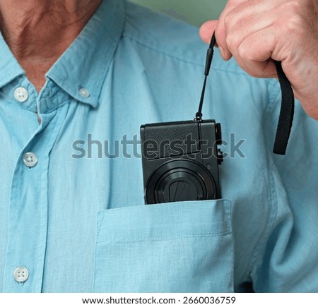 Small premium compact point and shoot digital camera. Being pulled from a mans shirt  breast pocket. Illustrates portability, convenience and discretion for everyday carry around photography. 